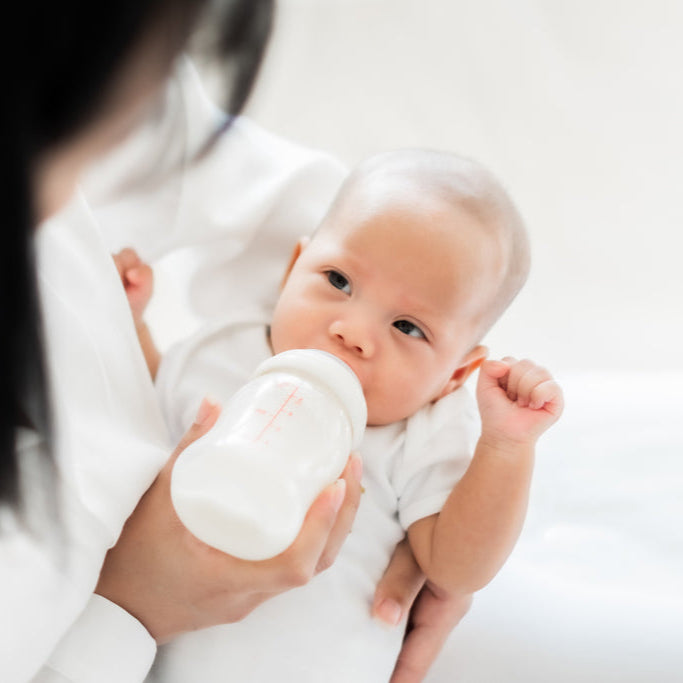 Baby being held by a person with a bottle on a white background